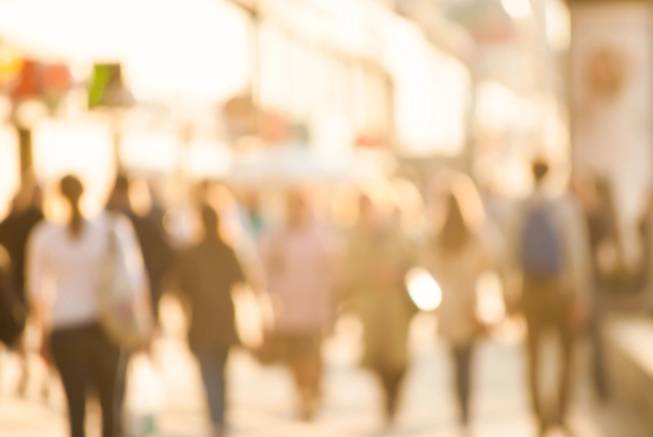 Blurred crowd walking in sunny street.